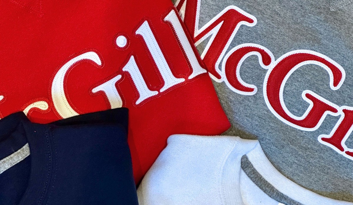 Close-up of four folded sweatshirts in different colors—red, gray, navy blue, and white—featuring large embroidered McGill logos in white and red lettering