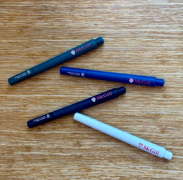 Set of four McGill-branded recycled pens in green, blue, black, and white, made in Canada, displayed on wooden surface.
