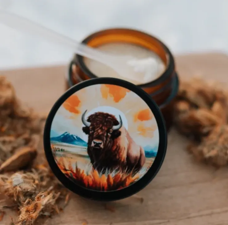 Amber glass jar with bison artwork on lid, displayed open with creamy wax and wooden scoop.
