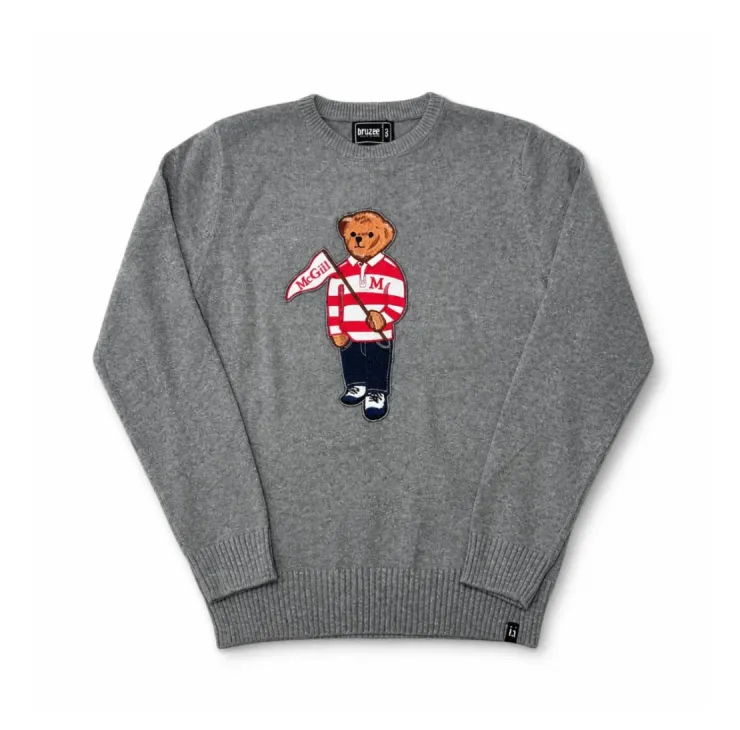 Grey knit McGill crewneck sweater featuring a bear appliqué dressed in a striped rugby shirt and holding a McGill pennant.