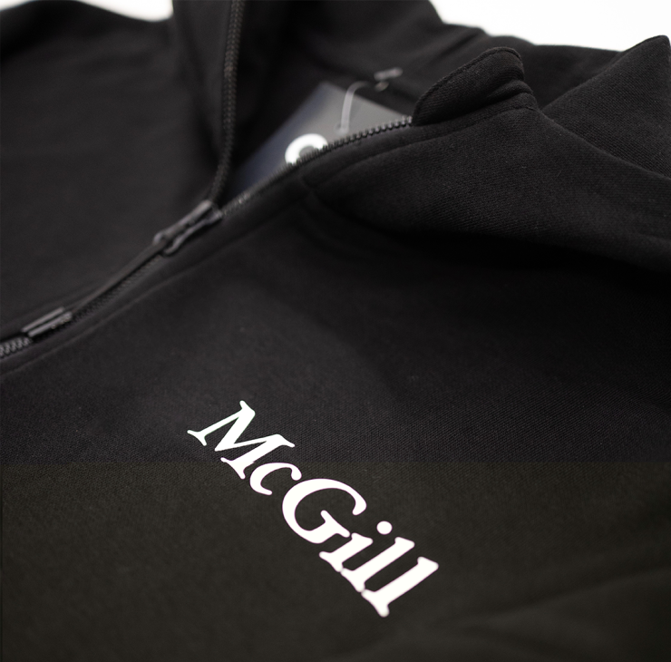 Close up of the white rubber printed McGill logo on the left chest of a black half-zip hoodie