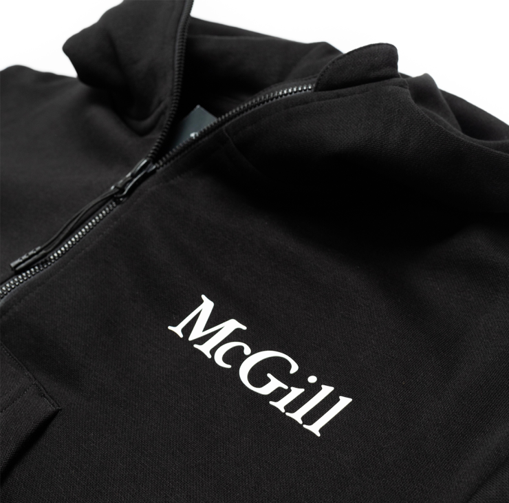 A close up of the white rubber printed McGill logo on the left chest of a cropped half zip hoodie