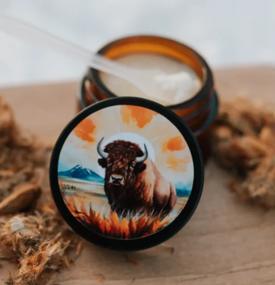 Amber glass jar with bison artwork on lid, displayed open with creamy wax and wooden scoop.