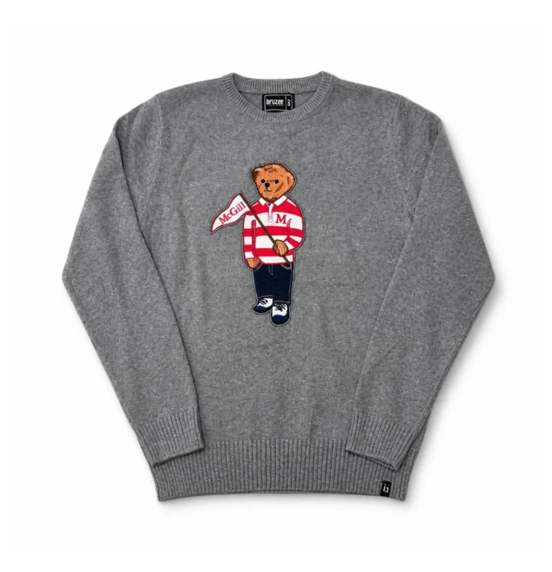 Grey knit McGill crewneck sweater featuring a bear appliqué dressed in a striped rugby shirt and holding a McGill pennant.
