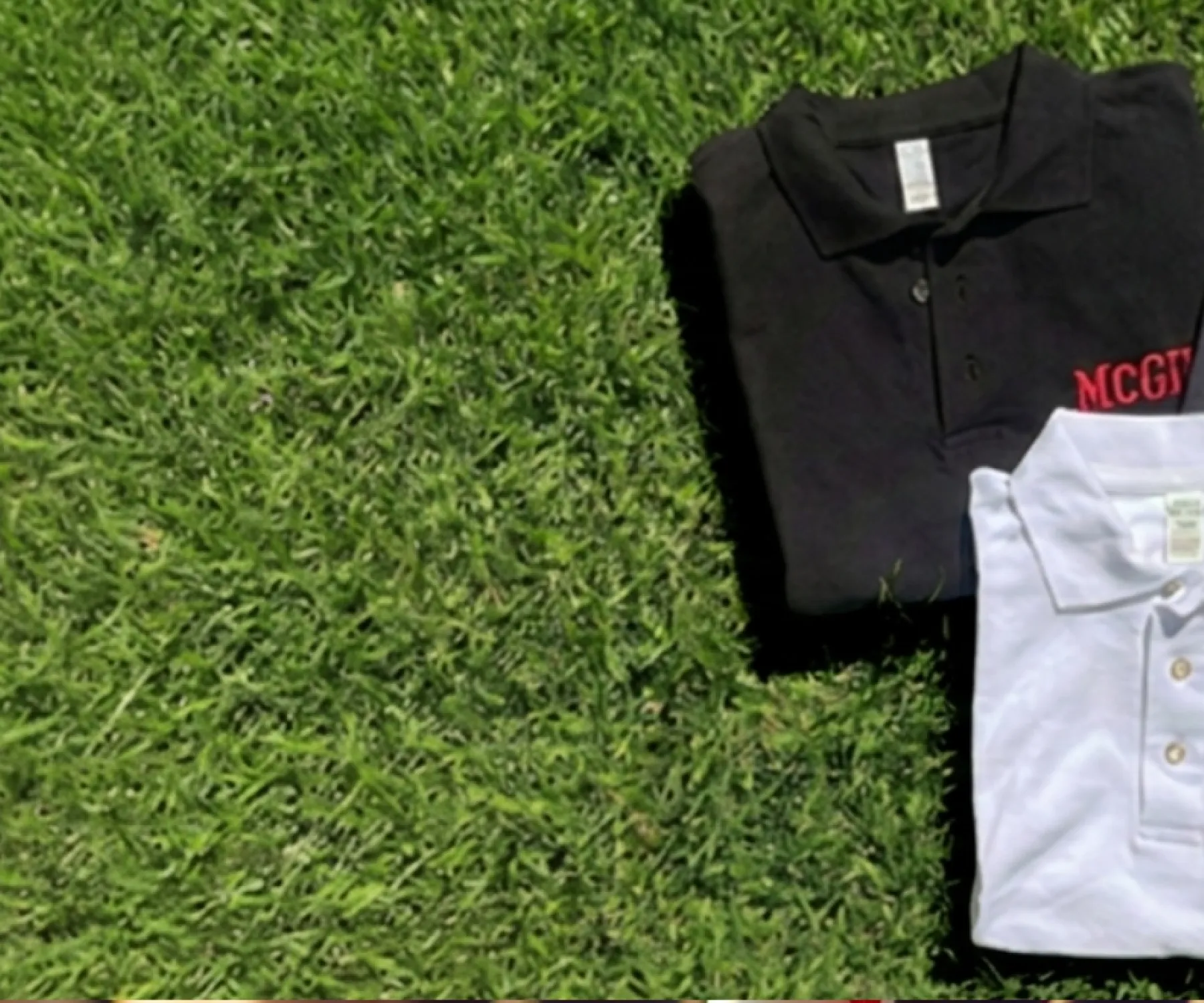 Folded McGill polo shirts in black, grey, and white with embroidered McGill logos, displayed on green grass background.