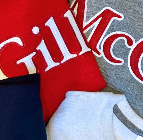 Close-up of four folded sweatshirts in different colors—red, gray, navy blue, and white—featuring large embroidered McGill logos in white and red lettering