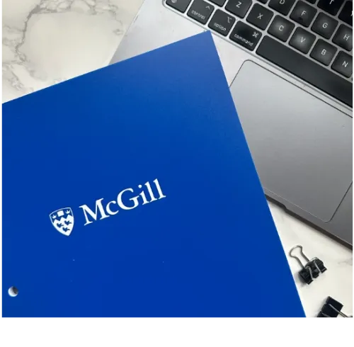 Blue McGill pocket folder with white McGill logo, shown beside a laptop on a desk surface.